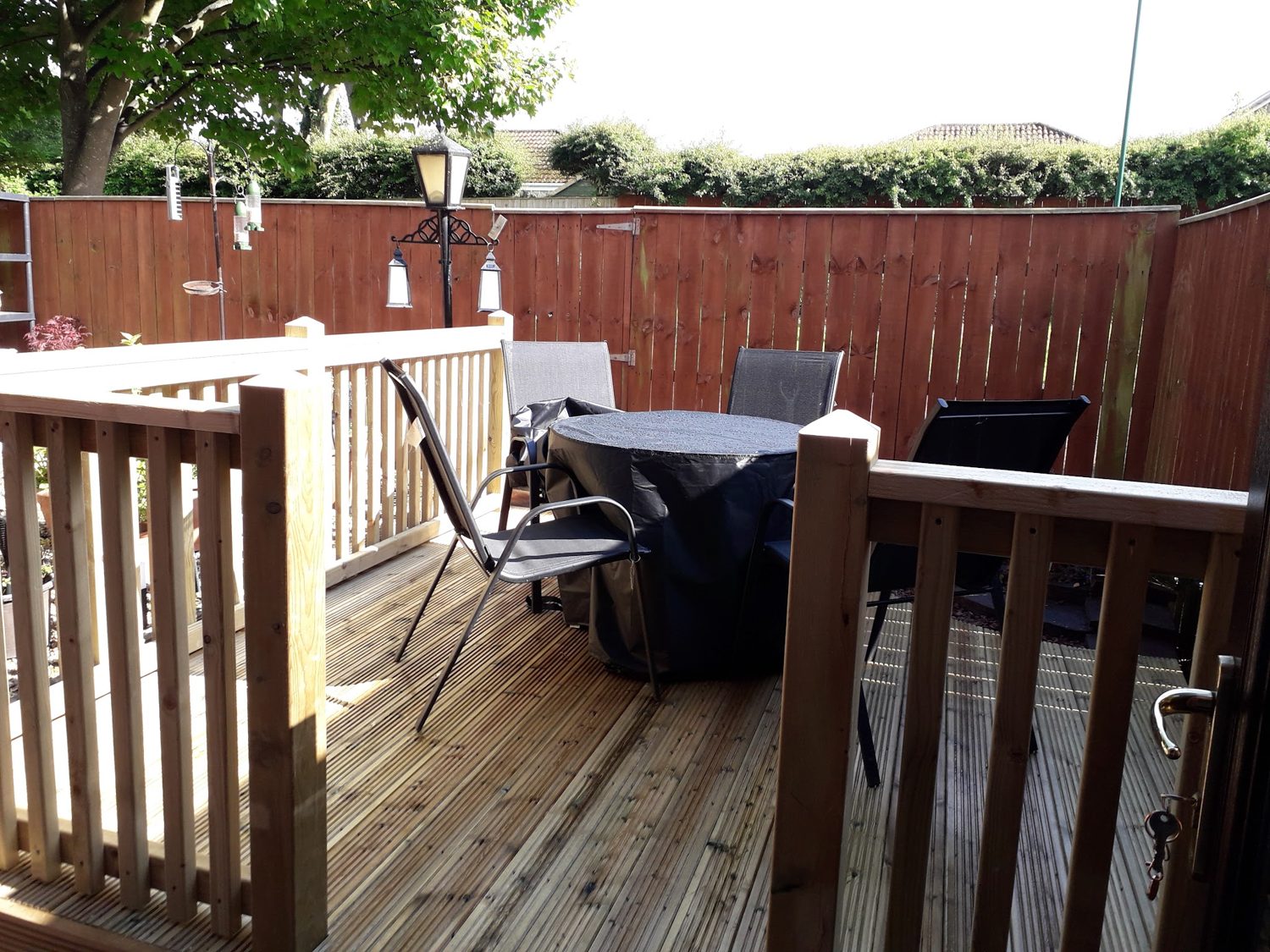 A deck with a balustrade, a table and chairs and a stained fence behind